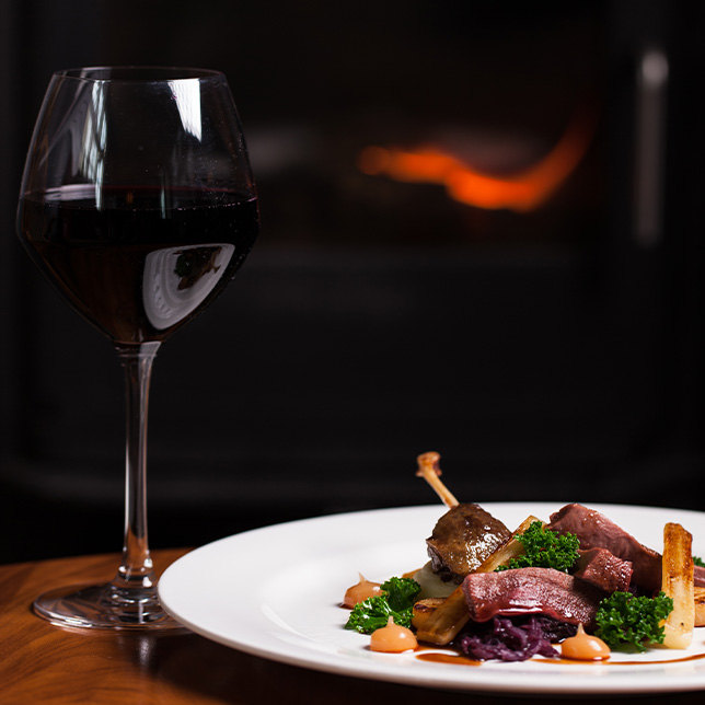 plate of duck with a glass of red wine next to it