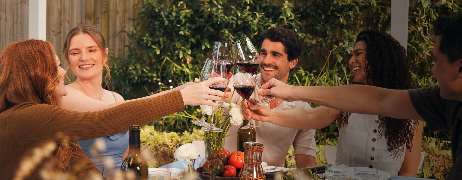 Table full of people and wine cheersing with red wine glasses