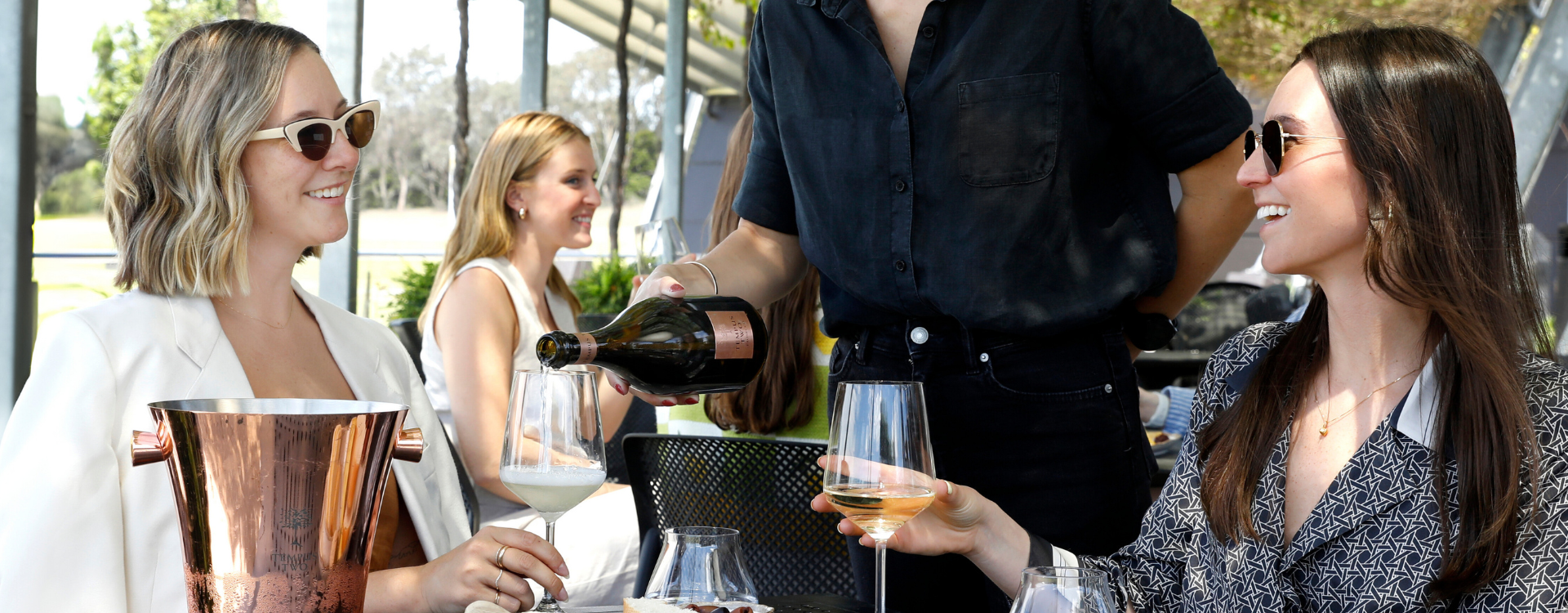 Two people outside drinking wine beneath the vines